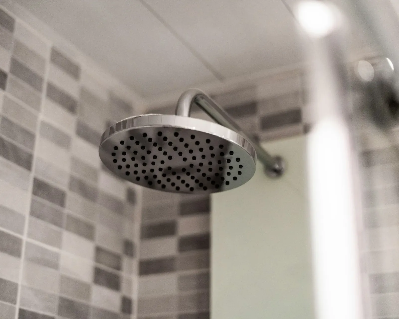 Chrome rain shower head running in a tiled bathroom