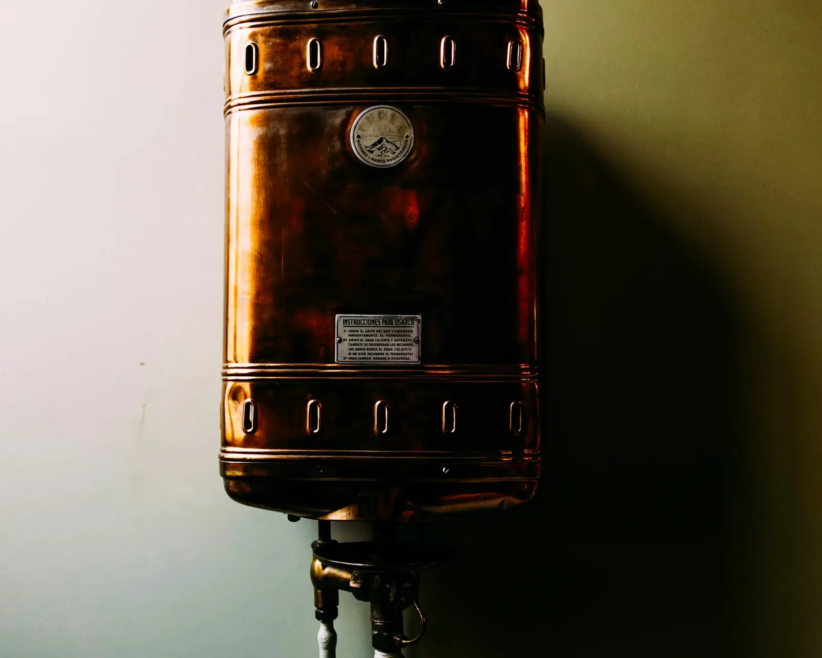 Copper water heater tank mounted on a dim wall