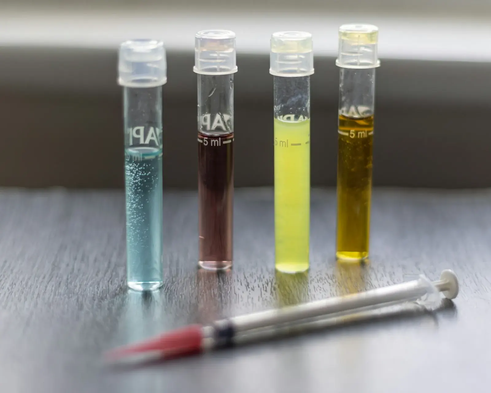 Test vials of colored water samples lined up beside a syringe