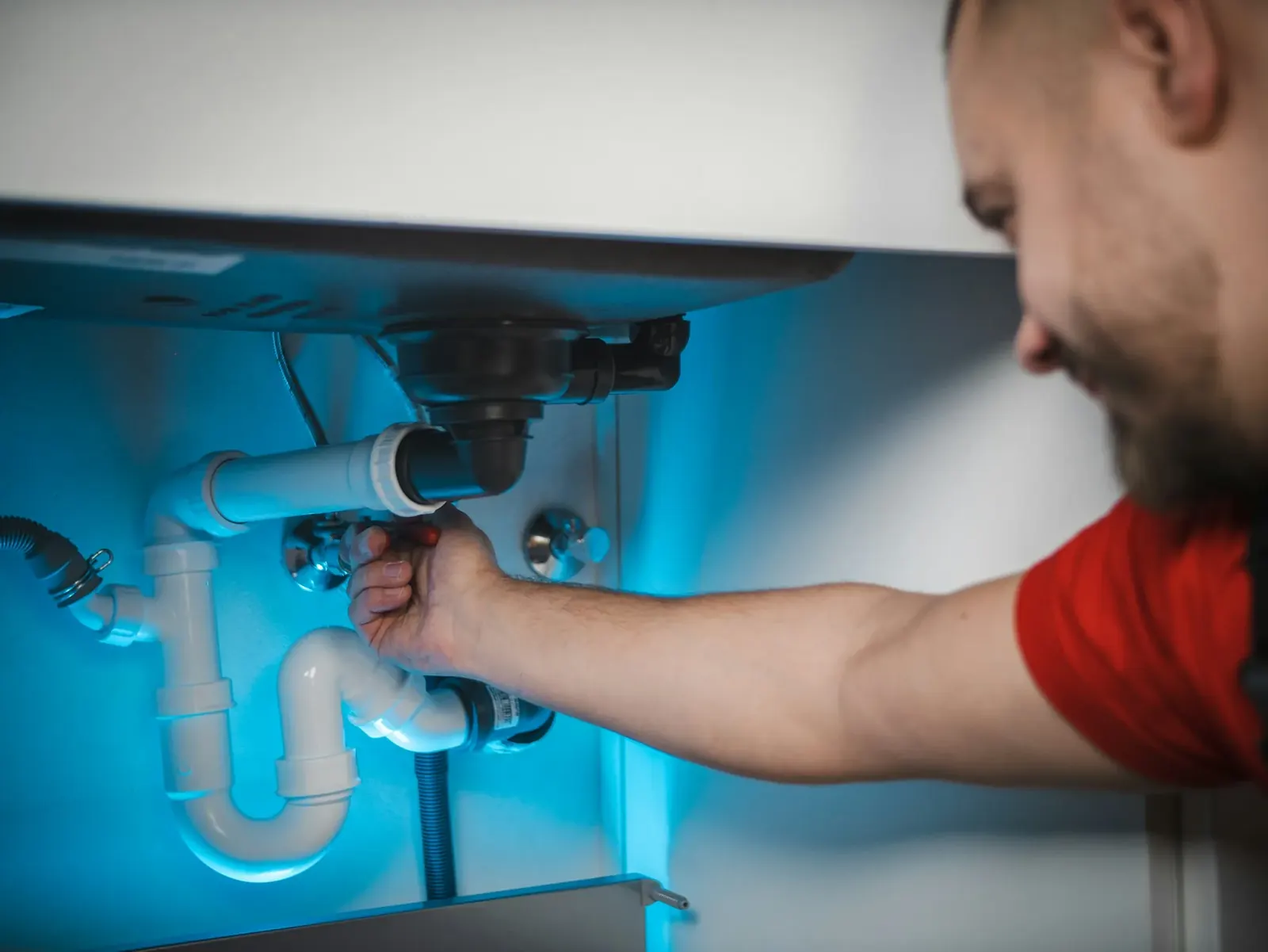 Plumber smiling while working on pipes under a kitchen sink