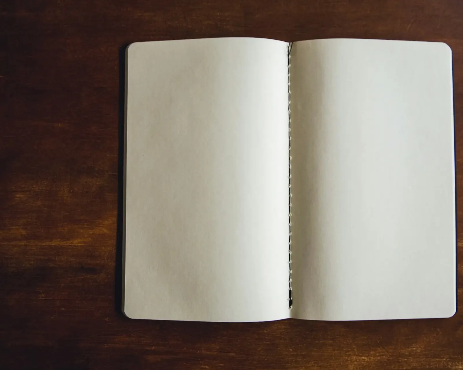 Open blank notebook lying on a dark wooden desk