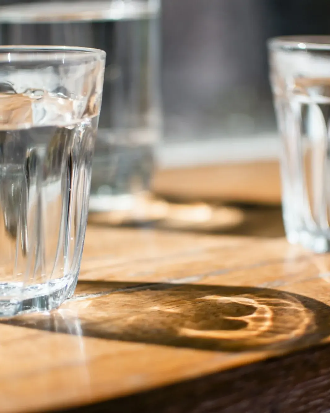 Two glasses of clear tap water on a wooden table in afternoon light