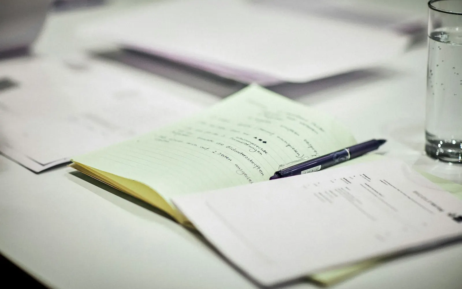 Printed documents and a pen on a desk beside a glass of water