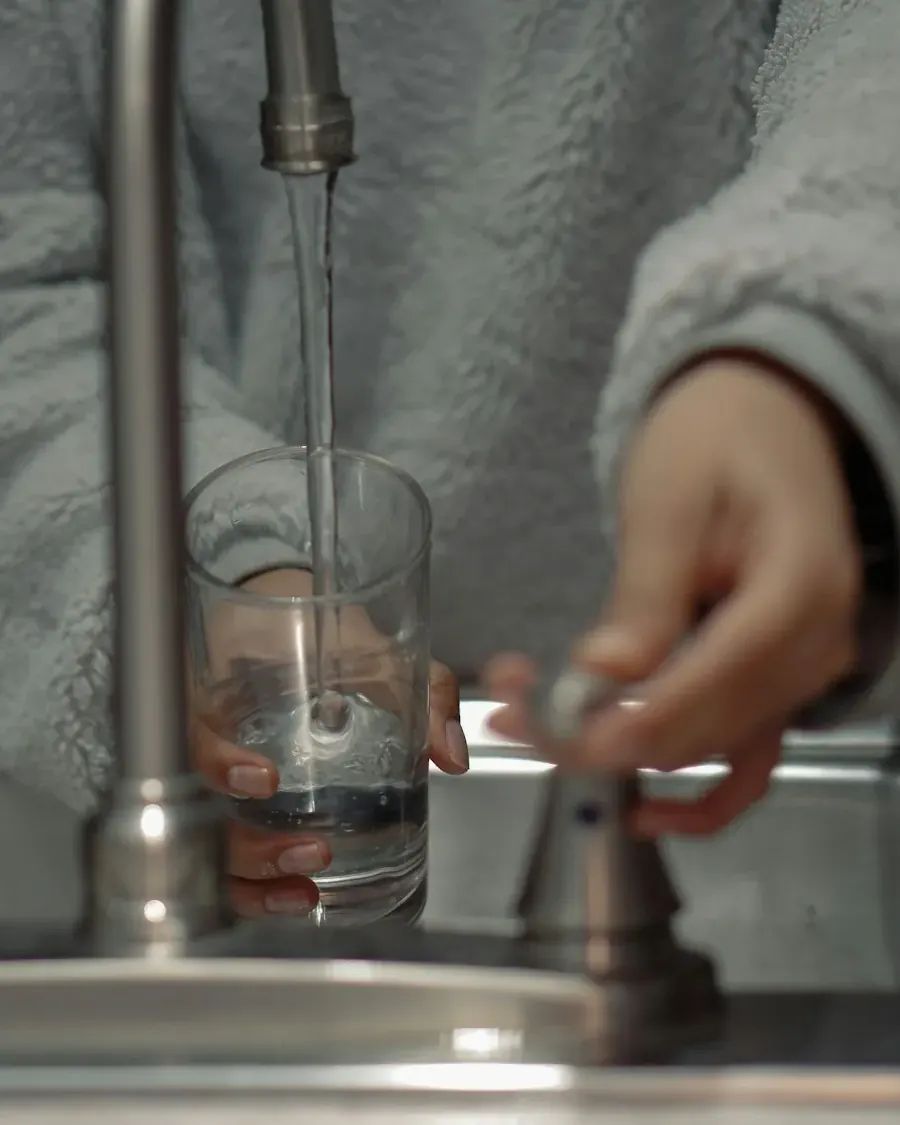 Person filling a glass of water at a stainless kitchen sink